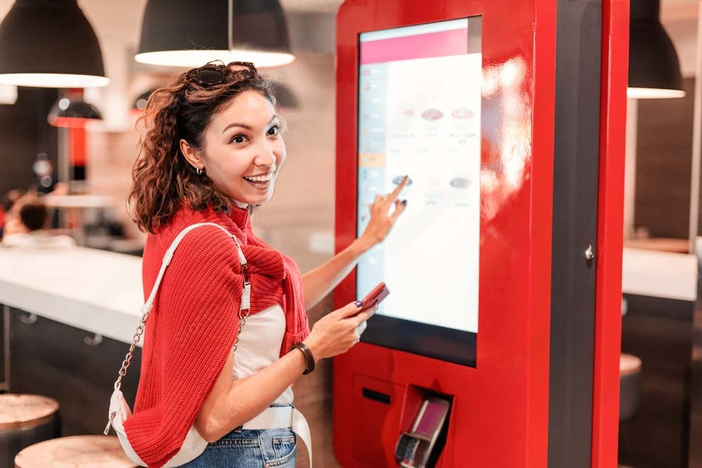 a woman in red ordering at a stand up menu kiosh